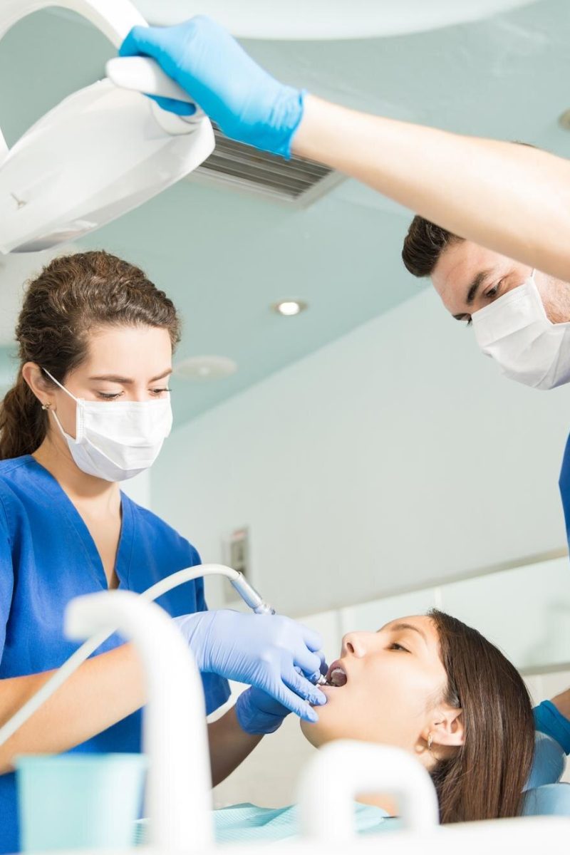 dentist-treating-patient-with-dental-tool-while-male-colleague-adjusting-light-clinic_662251-2544