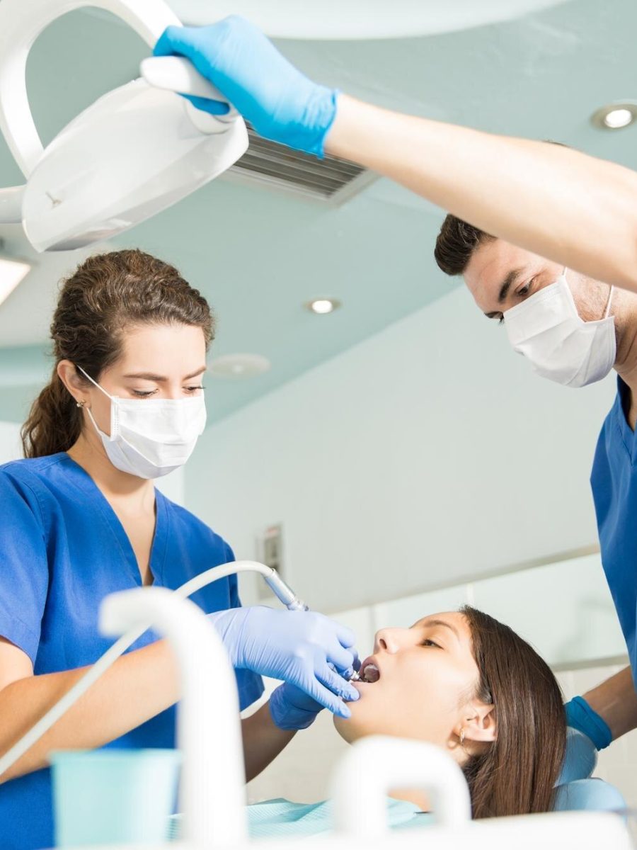 dentist-treating-patient-with-dental-tool-while-male-colleague-adjusting-light-clinic_662251-2544